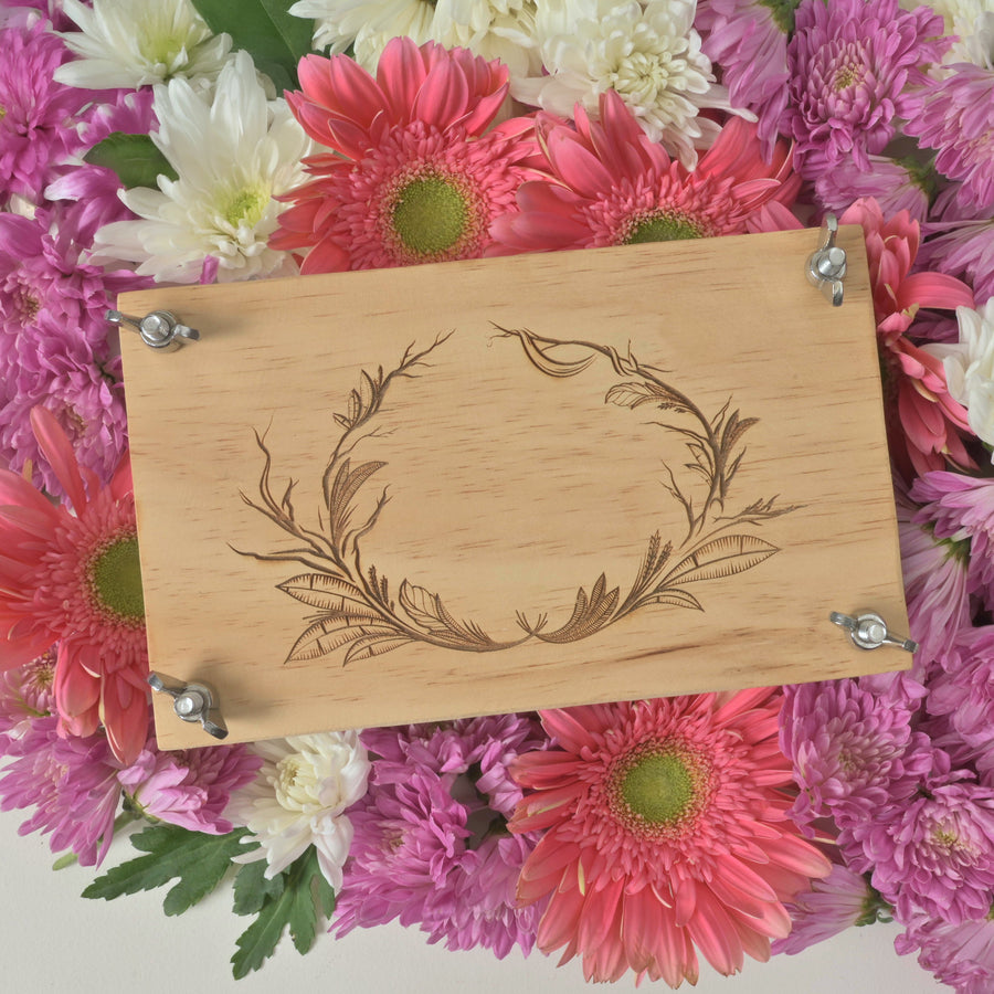 Engraved wooden flower press resting beside fresh pink and white blooms
