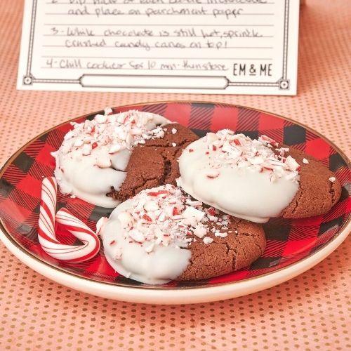3 peppermint cookies on a red flannel plate with candy cane and Em & Me Recipe Card in background
