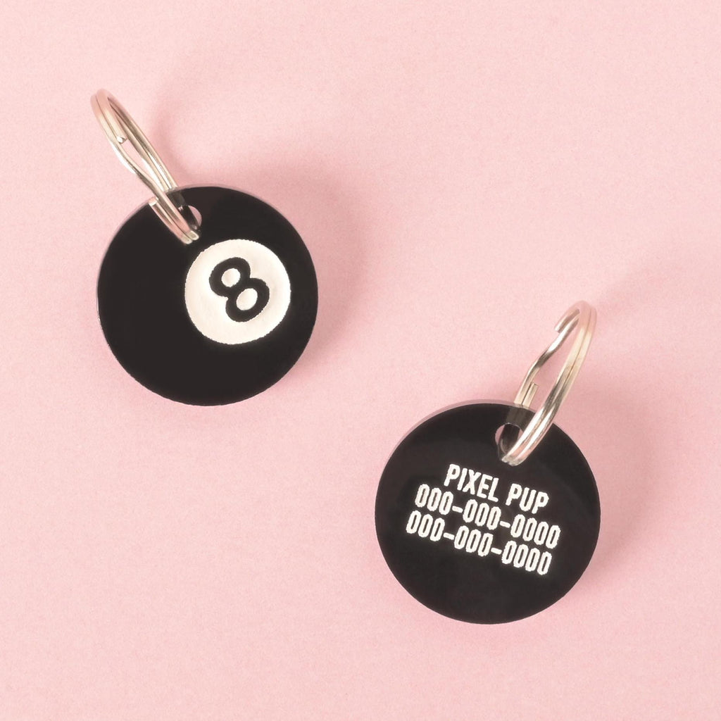 Front and back of black acrylic 8-ball pet ID tag with silver keyrings, showing number 8 on one side and custom engraved text on the other.