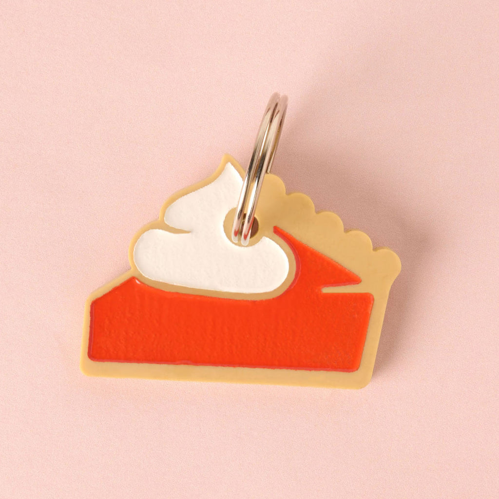 A novelty charm shaped like a slice of pie (pumpkin or sweet potato) made from layered acrylic in tan, orange/red, and white whipped cream. The charm is attached to a split ring.