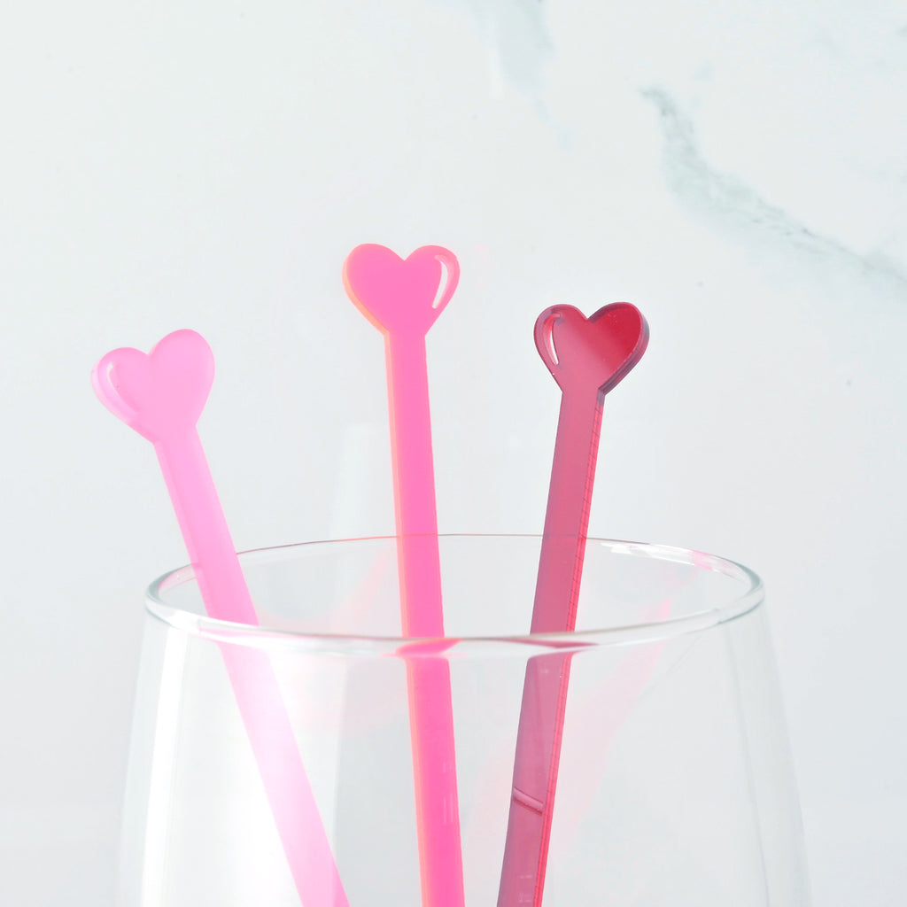 Close up of frosted pink, red and fluorescent pink tiny heart cocktail stirrers in a clear glass on marble background