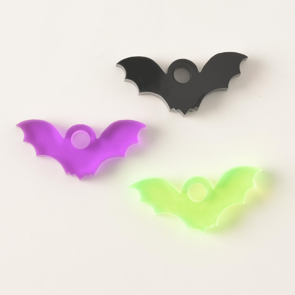 Three laser-cut acrylic bat-shaped charms on a white background: one black, one bright purple, and one fluorescent neon green.