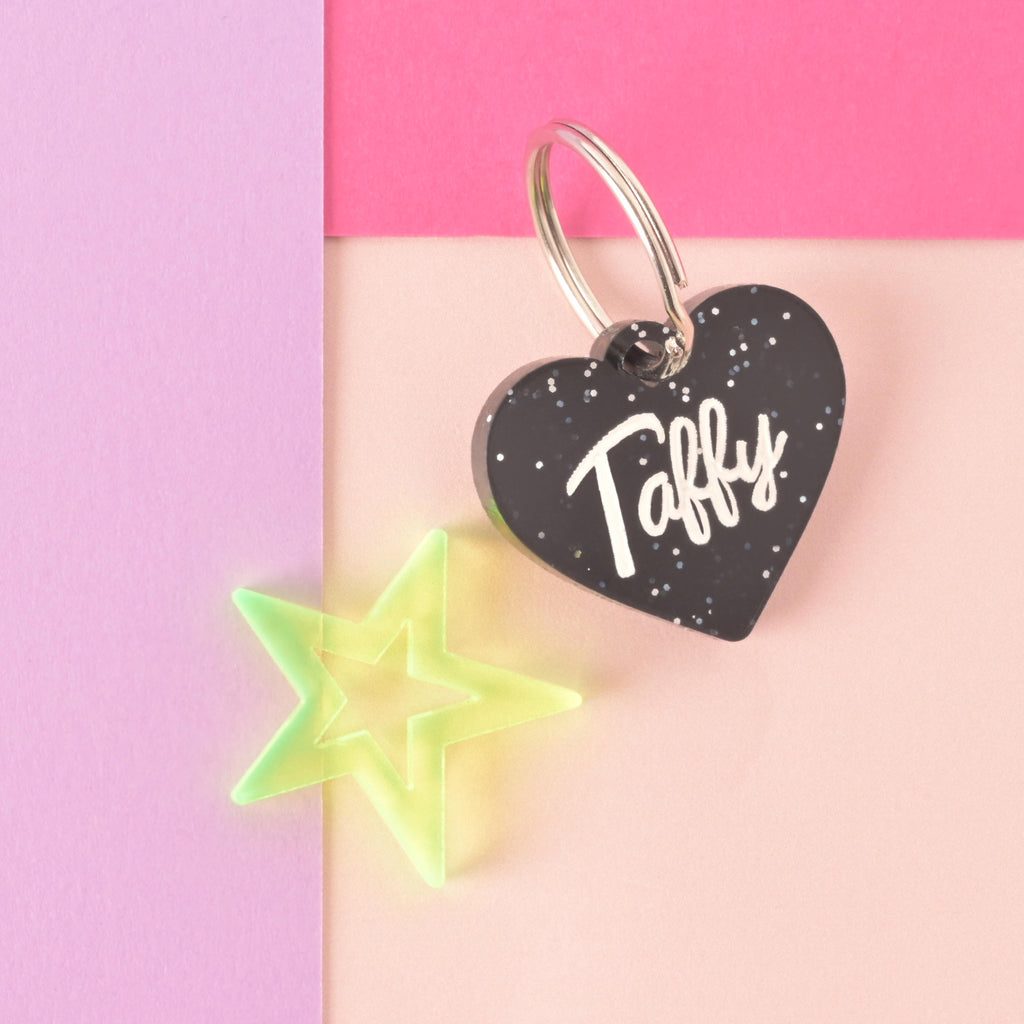 glitter black barbie inspired heart-shaped pet tag with a fluorescent green star mini charm off to the side on a color blocked background.