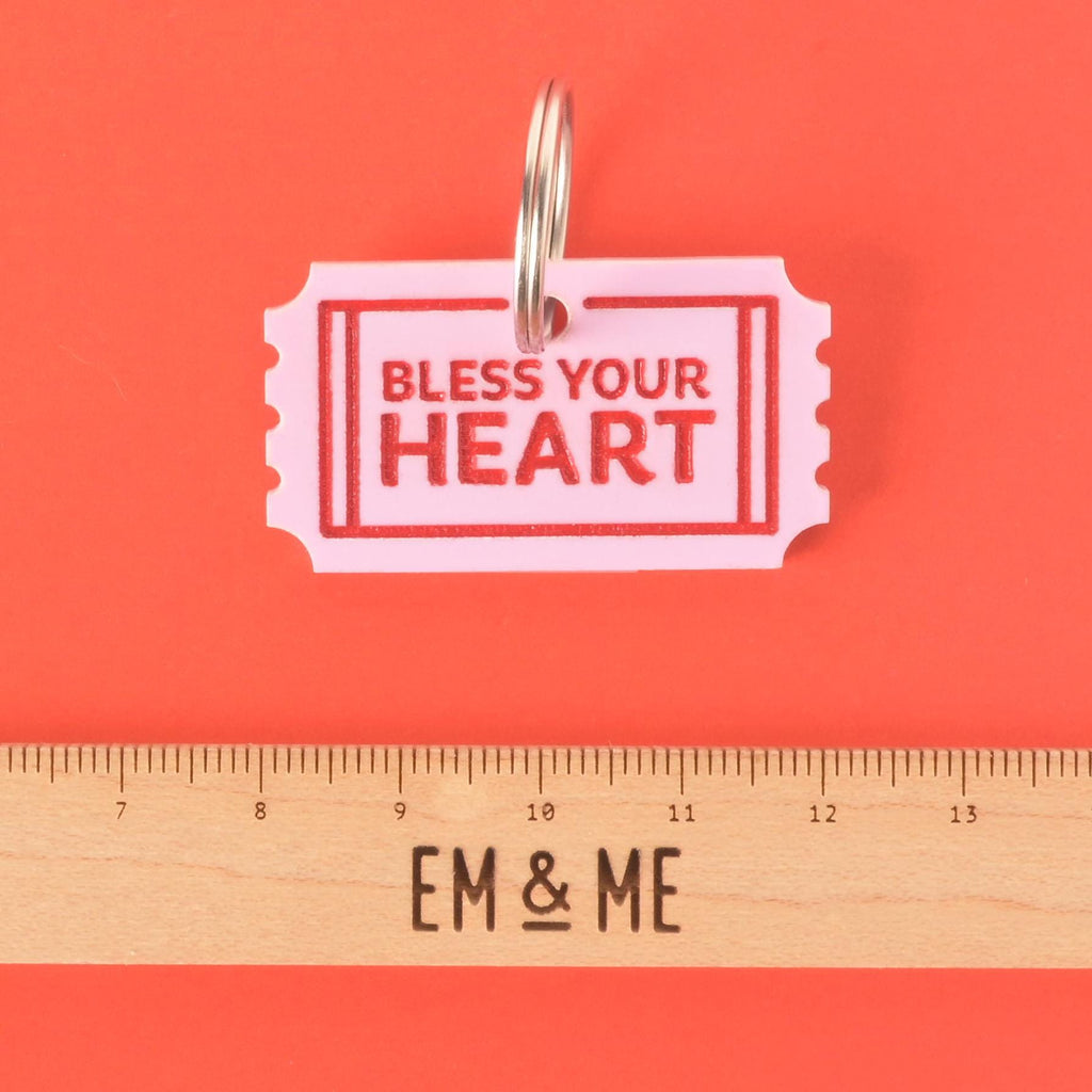 Bless Your Heart acrylic pet ID tag shaped like a pink ticket with red lettering, shown with ruler for size reference.