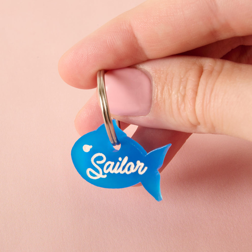 Little Fish Personalized name tag, Nautical Small fish Pet Tag, Tiny Tag, Blue Fish Cat or small dog breeds, XS personalized pet name tag Hand holding a blue fish-shaped pet ID tag with “Sailor” text, customizable charm for cats and dogs.