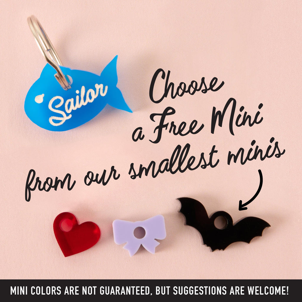 Blue fish-shaped pet ID tag with “Sailor” text, shown alongside mini add-on charms including a red heart, purple bow, and black bat, customizable accessories for dogs and cats.