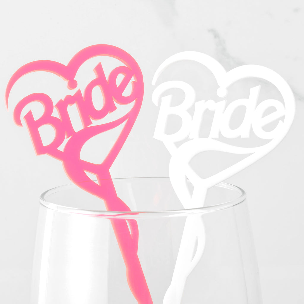 Close up of two Bride Barbie inspired cocktail stirrers in white and fluorescent pink. Stir sticks in a clear glass on marble background