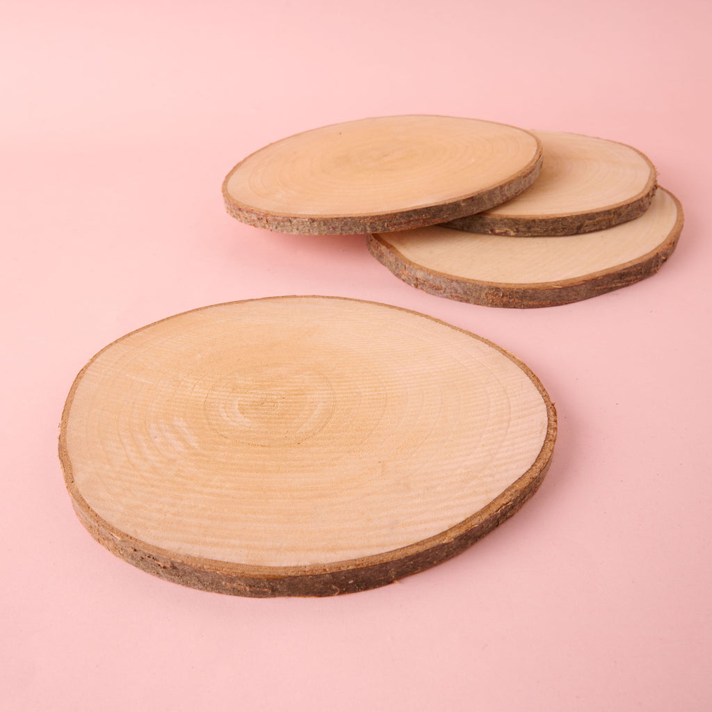 A small stack of large, circular natural wood slices with visible growth rings and natural bark edges. These unfinished wood discs are suitable for use as rustic centerpieces or trivets in home decor.