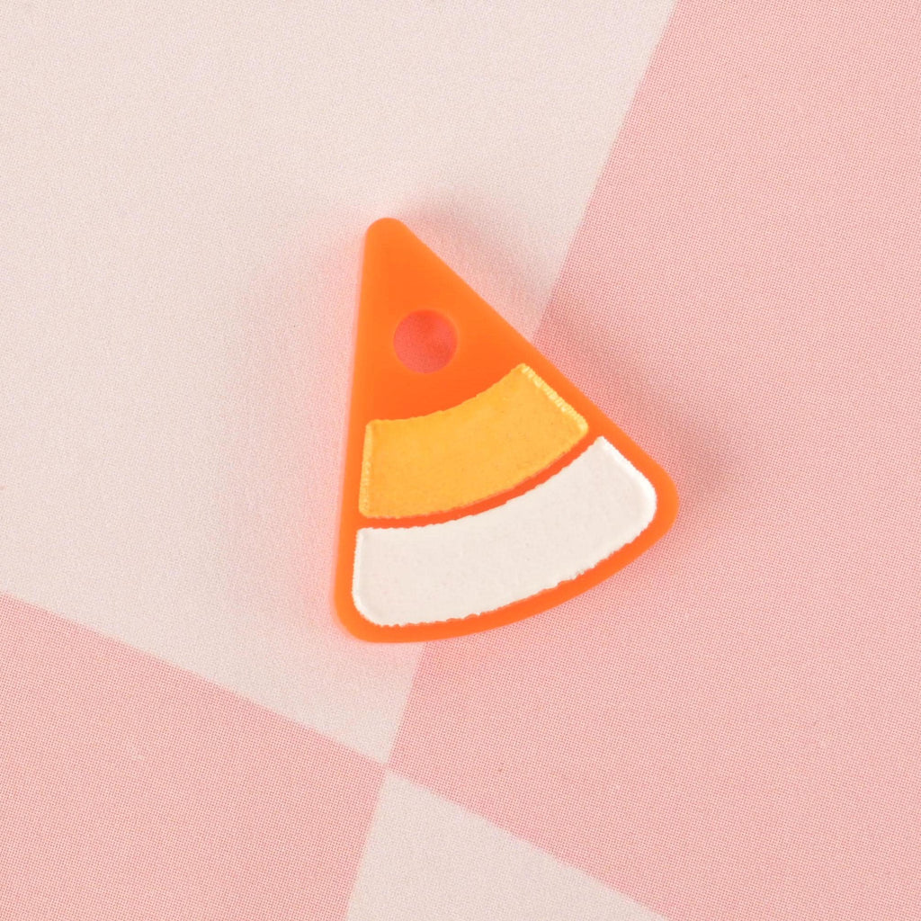 A single candy corn-shaped pet tag charm. The charm is orange, white, and yellow with a bright orange outline. It is displayed on a pink and white checkered background.