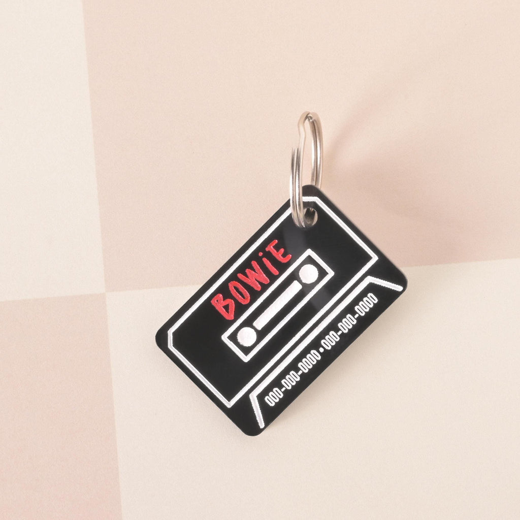 Black cassette tape shaped pet ID tag with customizable name and phone number, retro design for dogs and cats.