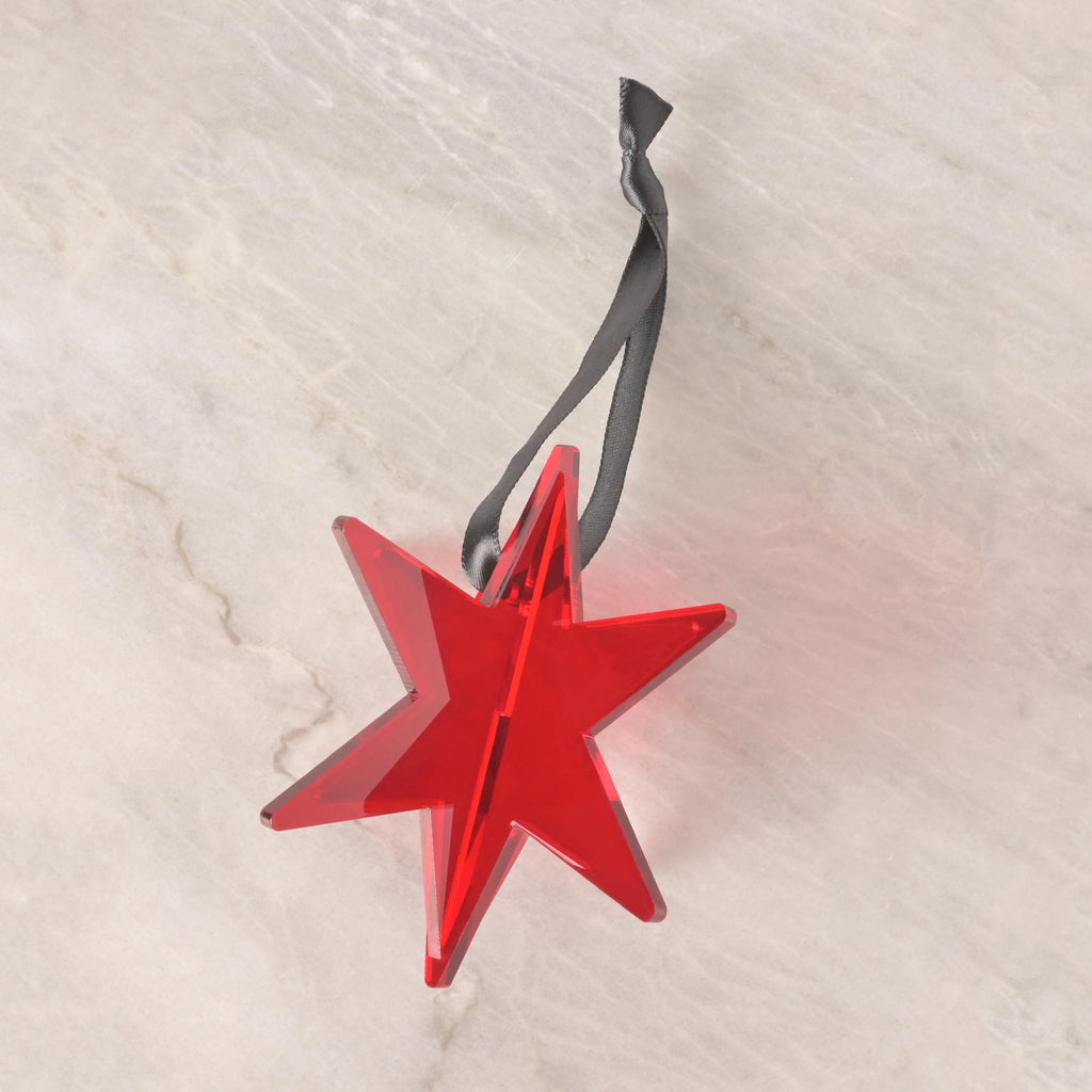 Red acrylic star ornament inspired by the Chicago flag, featuring a black ribbon for hanging, displayed on a neutral stone background.