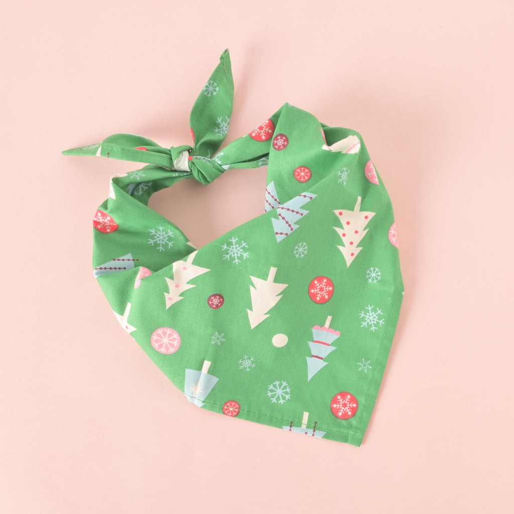 Green Christmas dog bandana with festive tree and snowflake print, tied neatly on a pink background for a holiday pet accessory display.