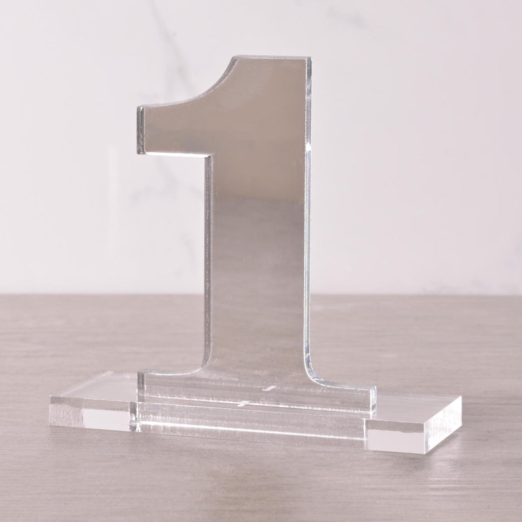 Freestanding clear acrylic table number “1” with a rectangular base, displayed on a neutral surface for weddings, parties, and events.
