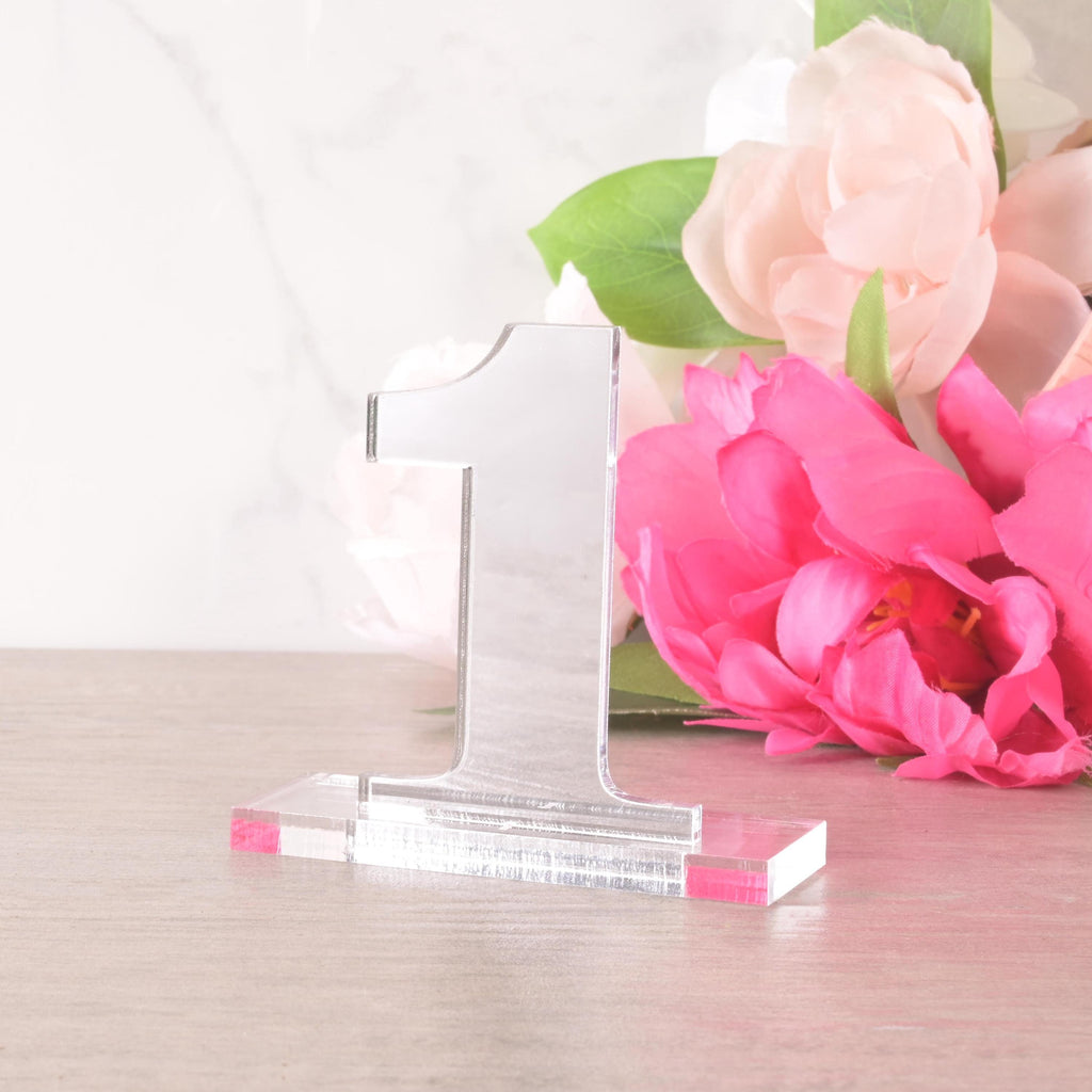 Freestanding acrylic table number “1” on a rectangular base, displayed with pink and white flowers, elegant modern wedding table décor.
