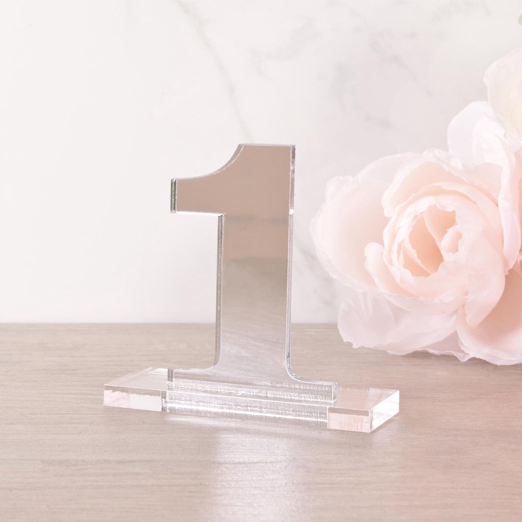 Transparent acrylic table number “1” on a clear base, styled with elegant white roses, modern minimalist wedding table decoration.