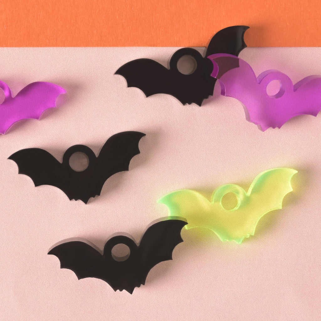 close up of a collection of bat-shaped seasonal mini charms in opaque black, fluorescent green and purple