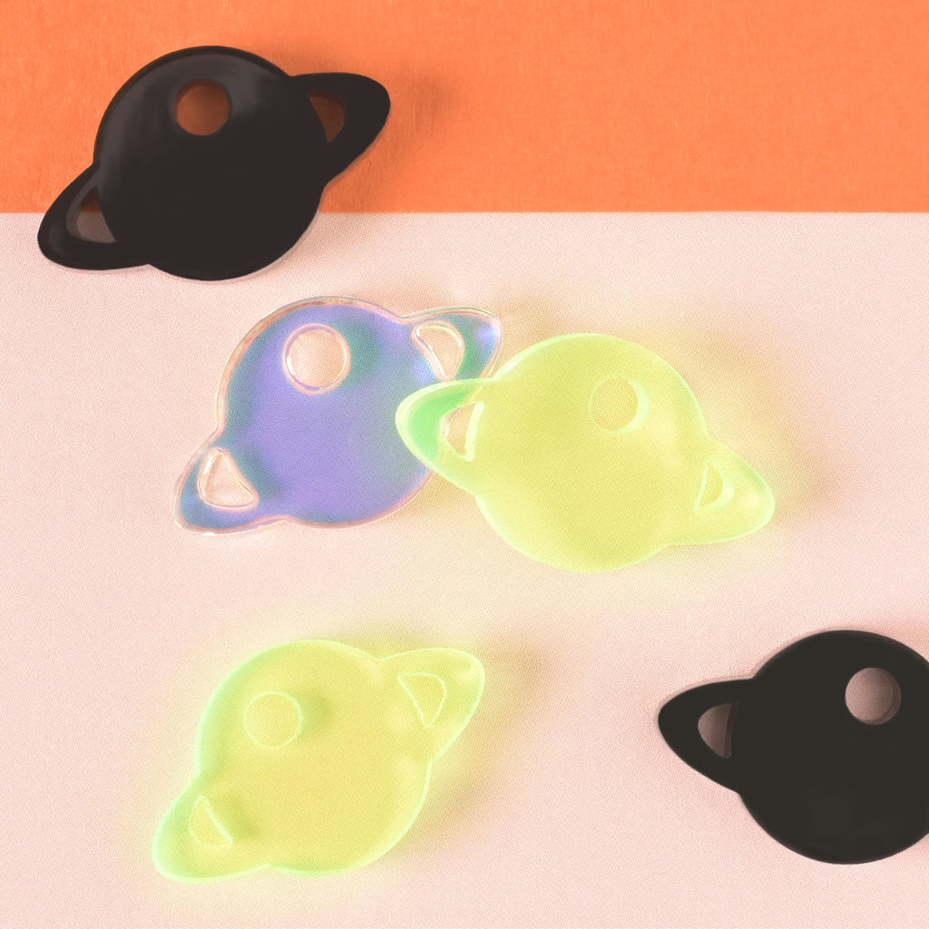 collection of Saturn-shaped mini charms for pet tags in black, iridescent and fluorescent green on color blocked background
