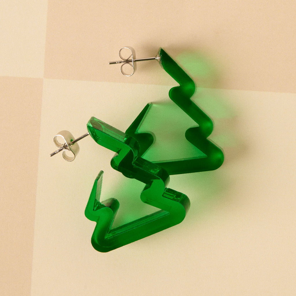 A pair of unique holiday earrings shaped like Christmas trees or zig-zag hoops in dark translucent green acrylic. The earrings are lightweight and displayed on a beige checkered background.