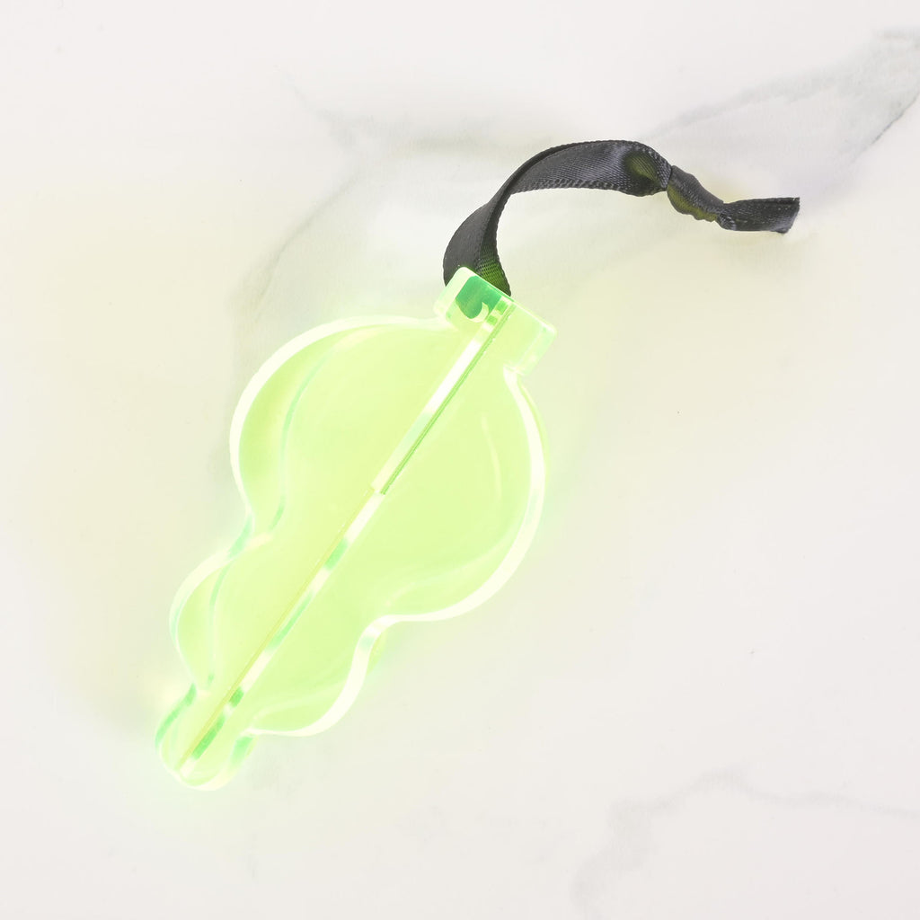 A fluorescent green, flat-pack Christmas tree ornament shaped like a classic glass ornament. The ornament is assembled and has a dark black ribbon tied to the top for hanging. The item is displayed on a white marble surface.