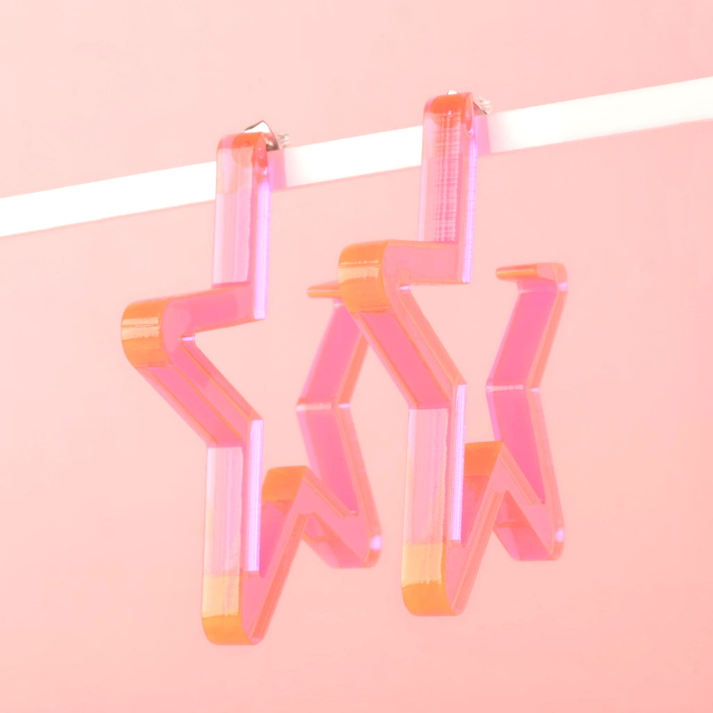 Fluorescent pink Star-shaped Hoop earring hanging in front of solid pink background.