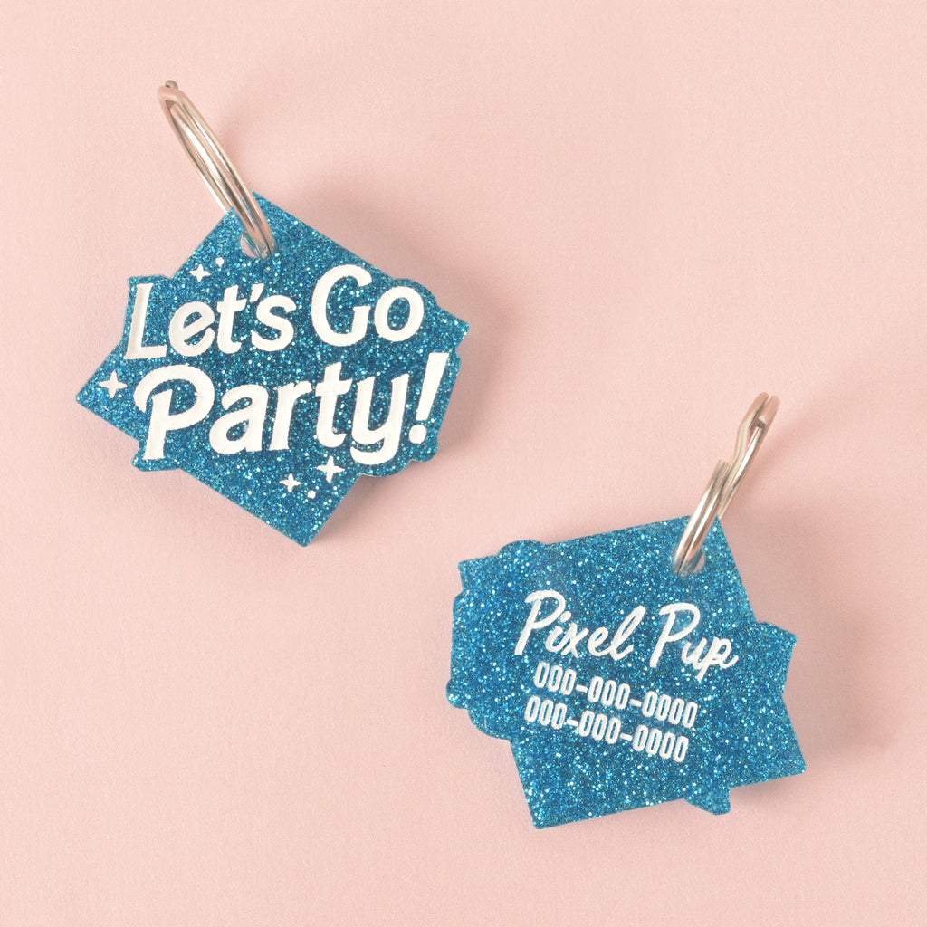 A product photo showing two sides of the same blue glittery, rhombus-shaped pet tag. The tag on the left shows the front with the words "Let's Go Party!" The tag on the right shows the back, which is custom engraved with the name "Pixel Pup" and two lines for phone numbers. Both tags have a silver split key ring attached.