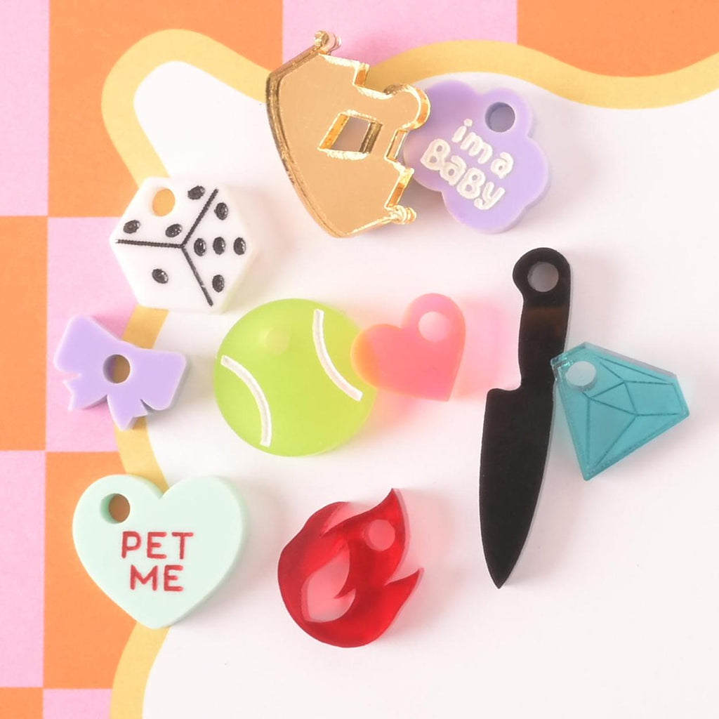 Assorted acrylic pet charms in shapes like tennis ball, diamond, dice, crown, bow, flame, and hearts for playful pet collar accessories.