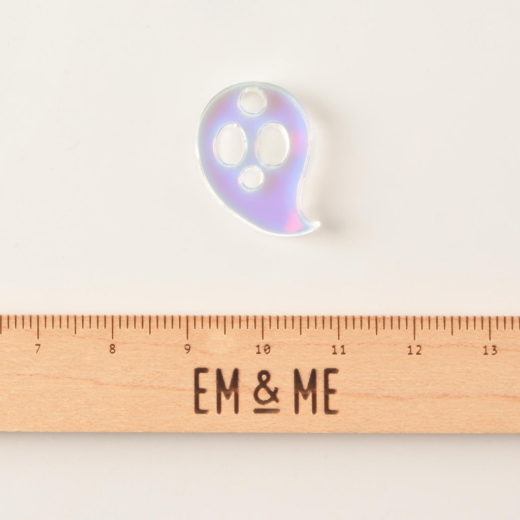 Iridescent ghost-shaped mini charm with hole for hanging on solid white background with wooden ruler that reads "EM & ME"