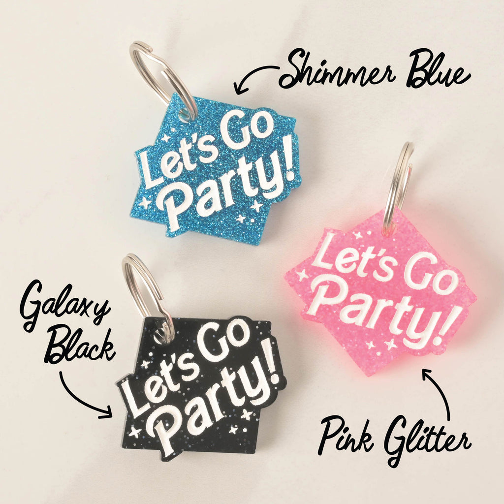 A product photo showing three glittery, rhombus-shaped pet ID tags. The tag at the top is blue glitter, labeled "Shimmer Blue." The tag on the bottom left is black glitter, labeled "Galaxy Black." The tag on the bottom right is pink glitter, labeled "Pink Glitter." All three tags are engraved with the words "Let's Go Party!" and have a silver split key ring.