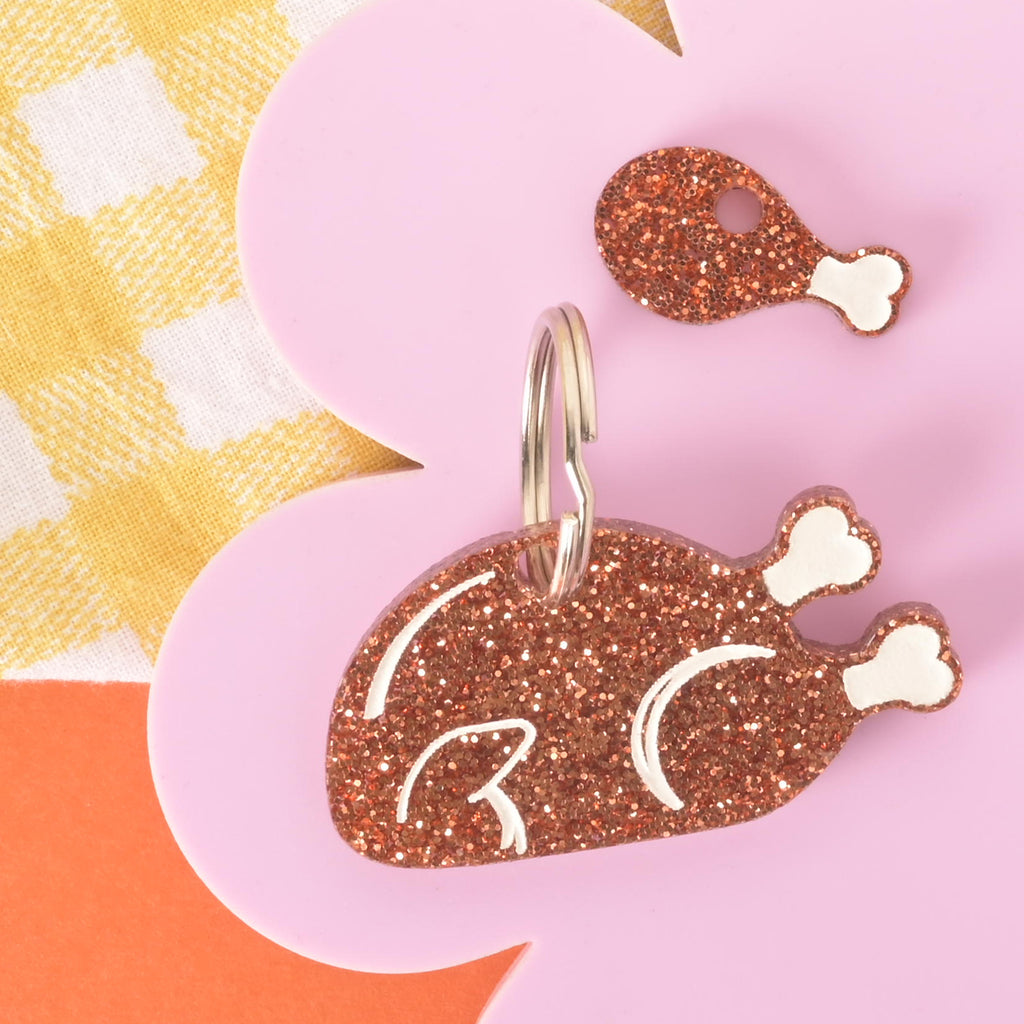 Brown glitter acrylic turkey pet ID tag with white bone details, engraved name, and phone number, shown with matching mini drumstick charm. Copper