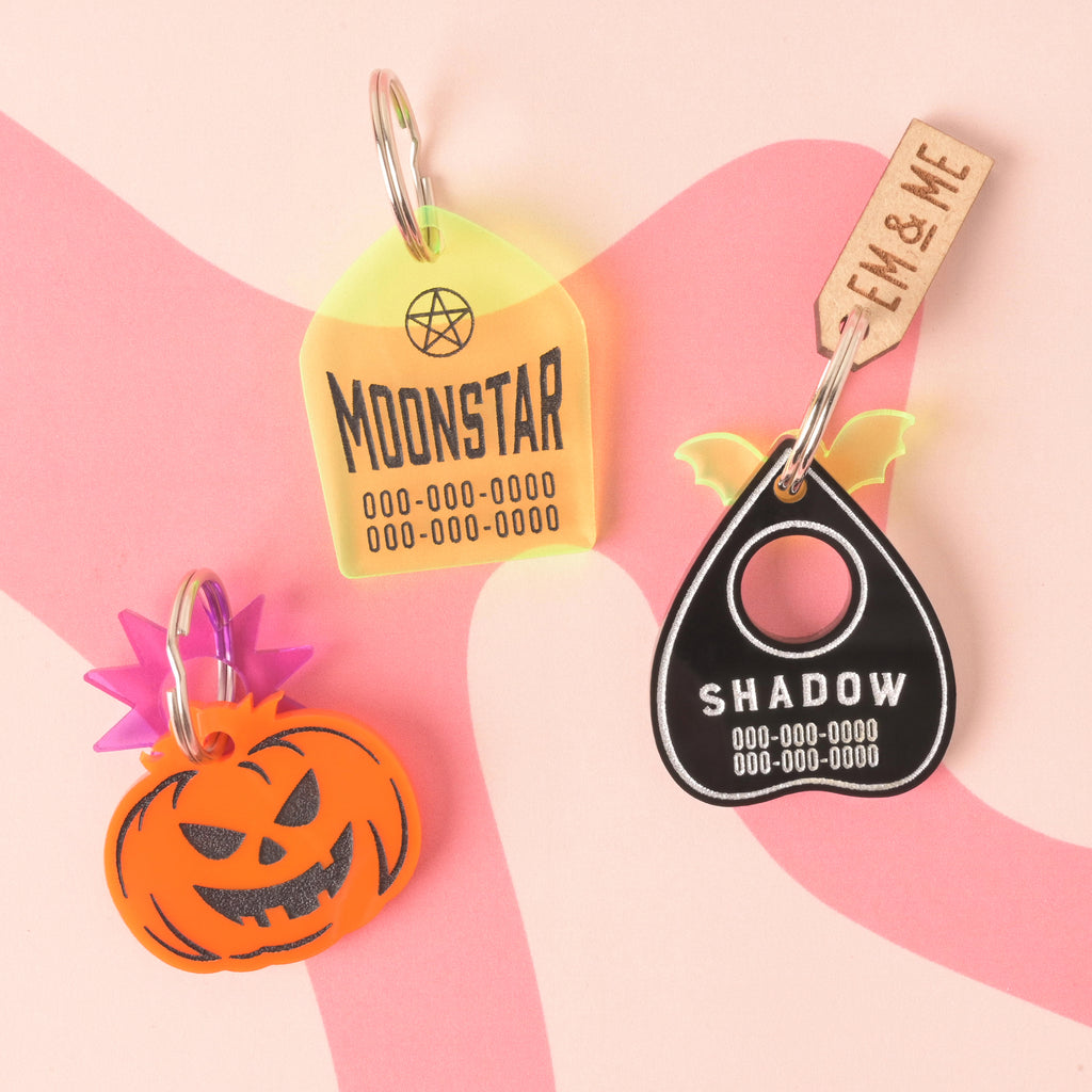Collection of three halloween themed pet ID tags. Fluorescent green Grave stone, orange jack-o-lantern and black ouija planchet on wavy pink background