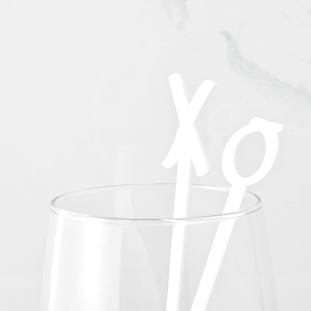 Close up of two hand drawn love cocktail stir sticks in a clear glass. X and O shaped stirrer on marble background