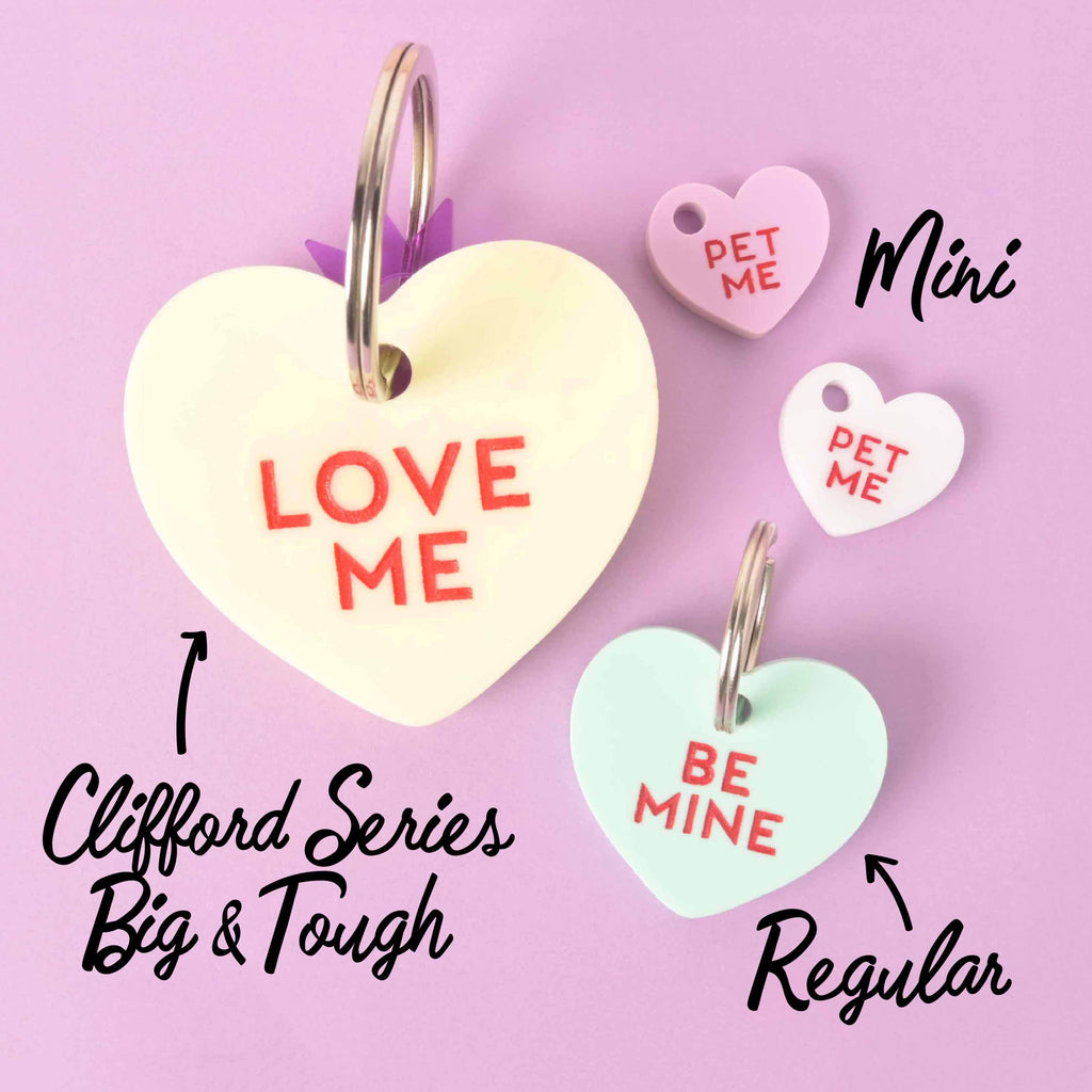 Heart-shaped pet ID tags in pastel colors with phrases Love Me, Be Mine, and Pet Me, shown in mini, regular, and Clifford big sizes.