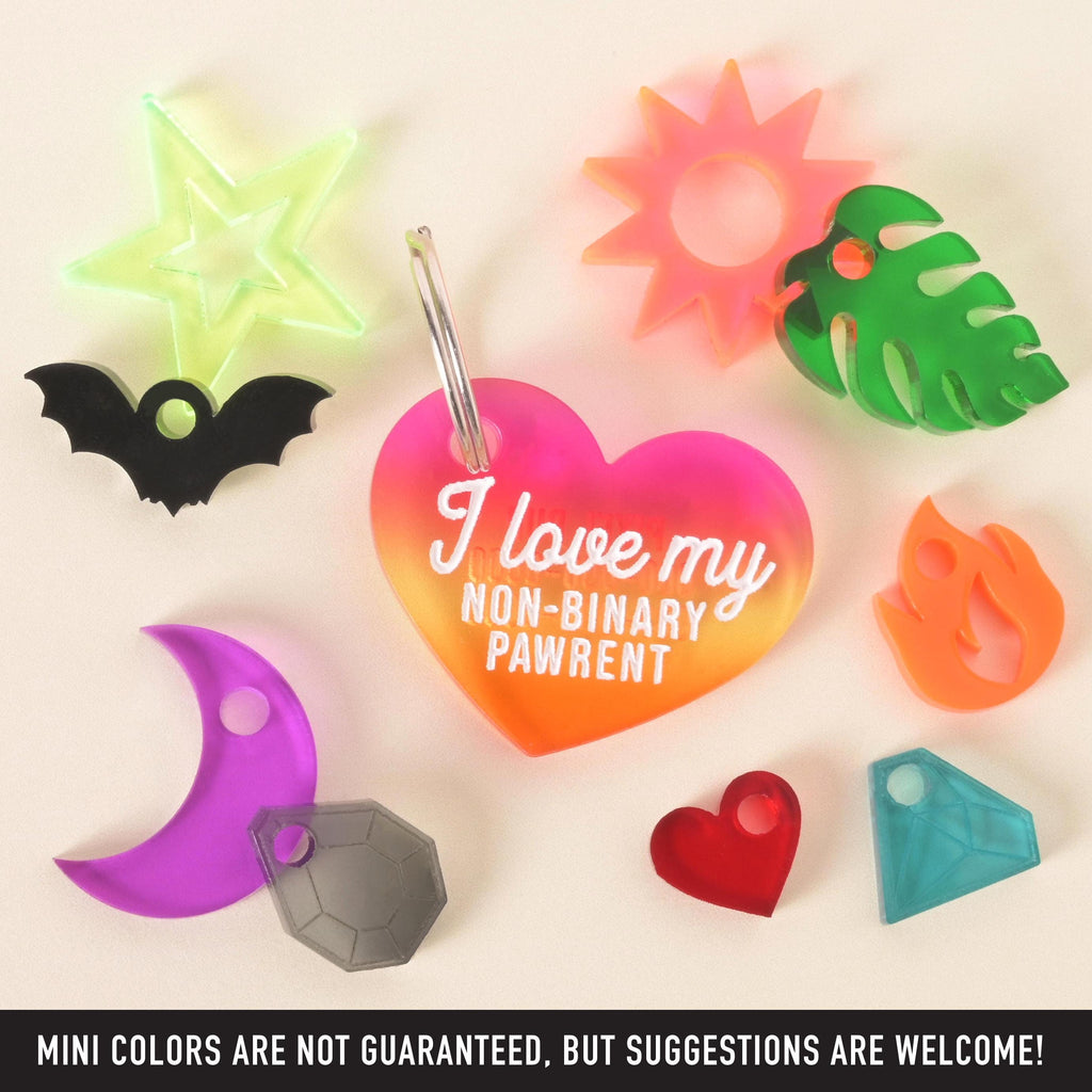 Rainbow gradient heart-shaped pet ID tag with white text that reads “I love my non-binary pawrent,” displayed with assorted colorful mini charm add-ons including a star, sun, moon, flame, leaf, heart, gem, and bat. Fun LGBTQ+ pride accessories for dogs and cats.