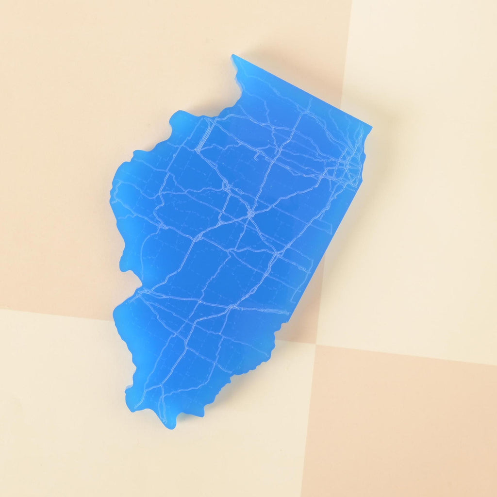 Blue acrylic coaster shaped like the state of Illinois with engraved roadway design, displayed on a checkered background.