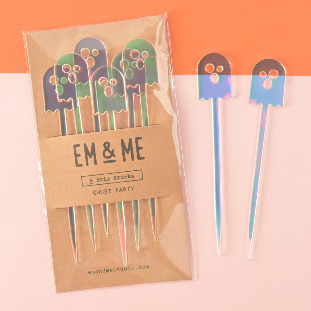 Set of 6 iridescent ghost-shaped cocktail stir sticks packaged on brown kraft paper on color blocked background

