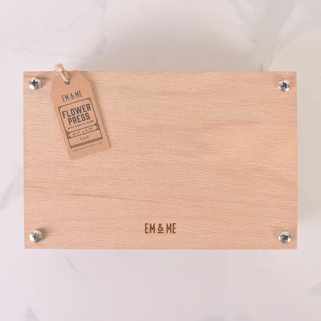 Rectangular wooden flower press engraved with EM & ME logo, secured with four metal bolts, and labeled with a kraft tag for DIY flower preservation.