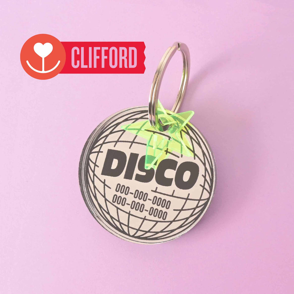 A product photo of a round, silver and black pet ID tag with a disco ball design and the word "DISCO" engraved on it. The tag is attached to a silver split key ring with a small, translucent neon yellow star. A red and white banner in the top left corner features a heart icon and the name "Clifford."
