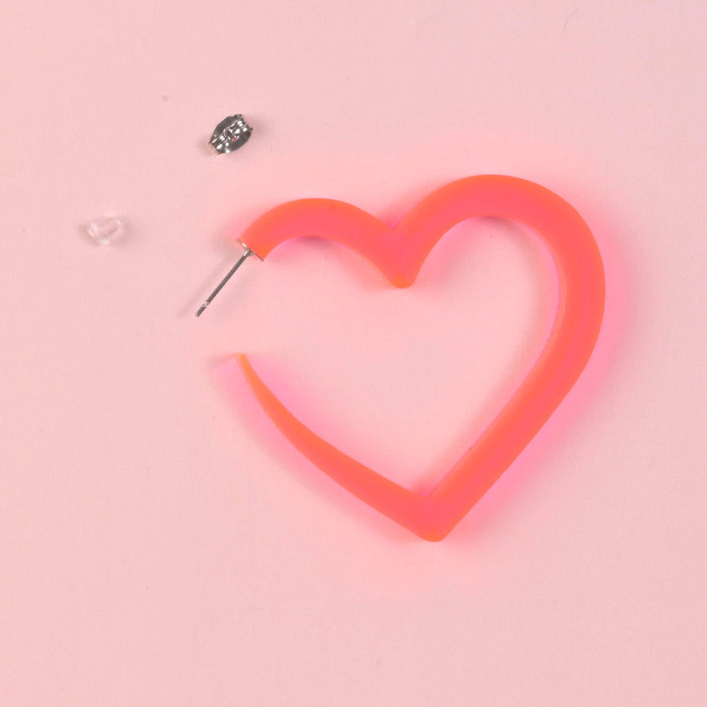 A single oversized, fluorescent pink acrylic heart-shaped hoop earring, shown with its silver post, metal butterfly backing, and clear rubber backing for closure.