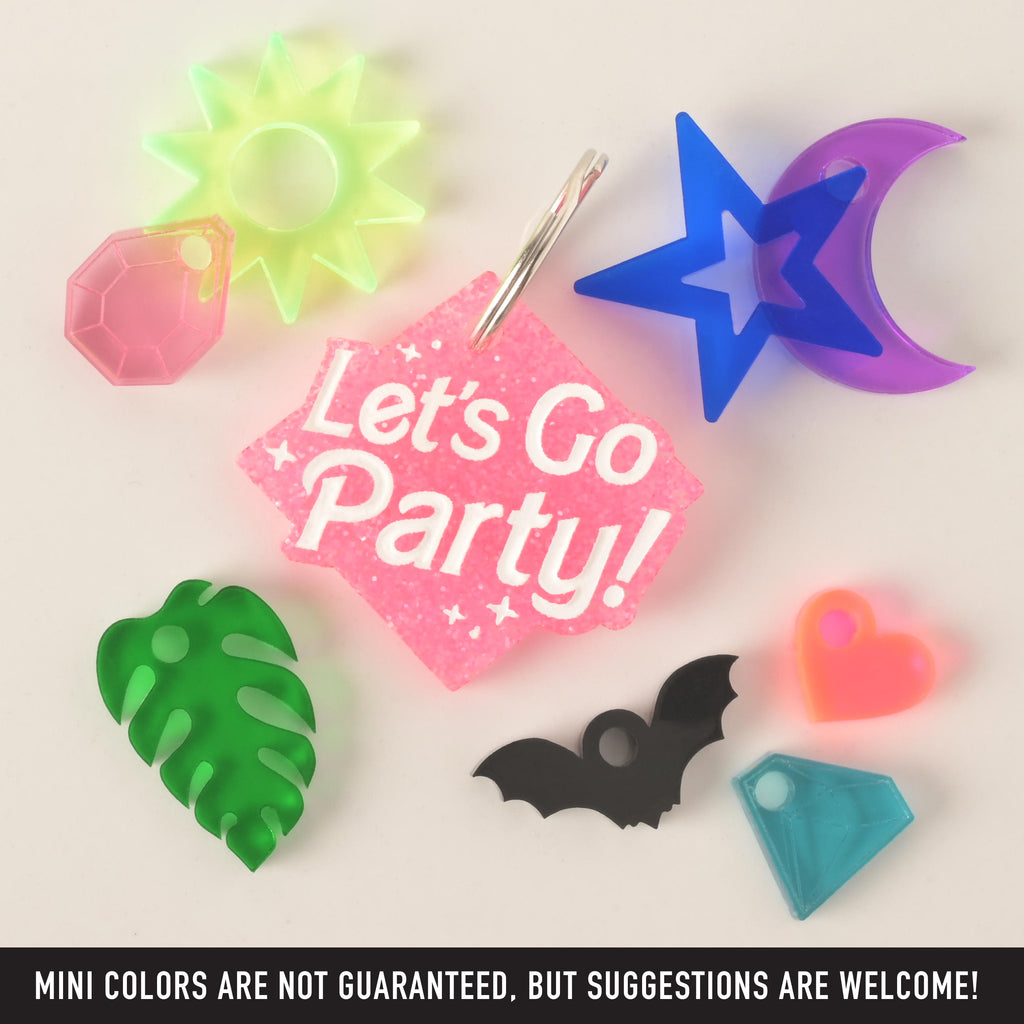 A product photo of a pink glittery, rhombus-shaped pet ID tag with the words "Let's Go Party!" in the center. Surrounding the main tag are several small, colorful charms: a neon green sun, a pink faceted gem, a blue star, a purple crescent moon, a green monstera leaf, a black bat, a neon orange heart, and a light blue geometric gem. Text at the bottom of the image reads, "MINI COLORS ARE NOT GUARANTEED, BUT SUGGESTIONS ARE WELCOME!"