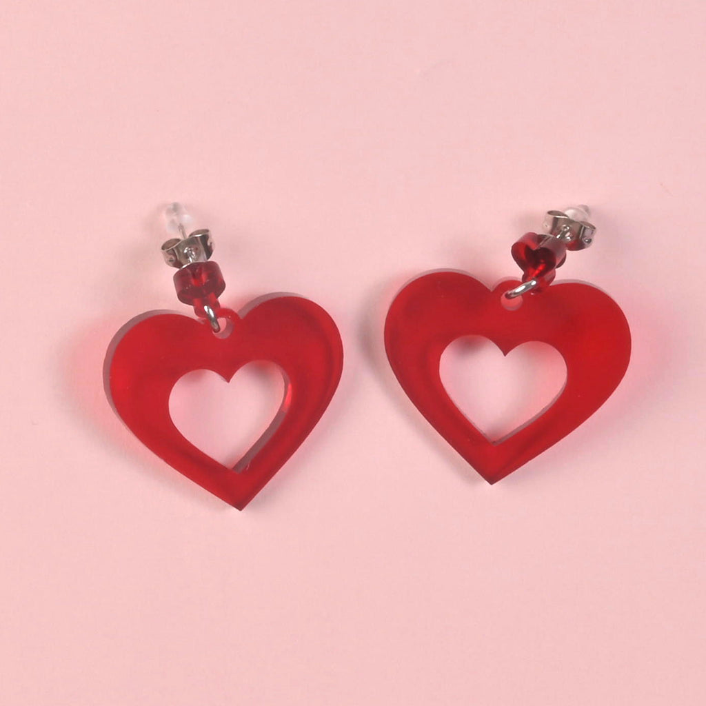 Red acrylic heart dangle earrings with a hollow center. Statement jewelry for a vibrant and romantic look.