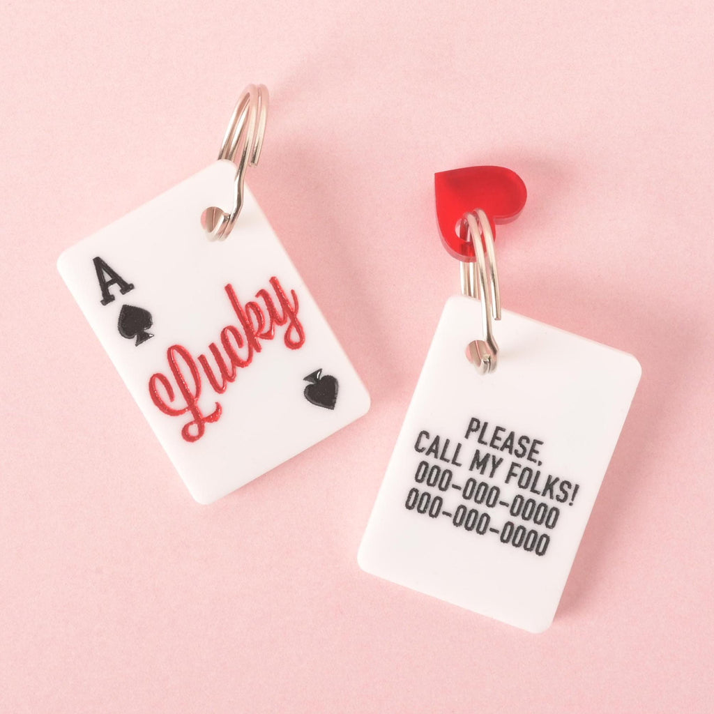 Two Lucky Ace pet tags shown on a pink background: front has “Lucky” in red with spade accents, back engraved with custom contact info.
