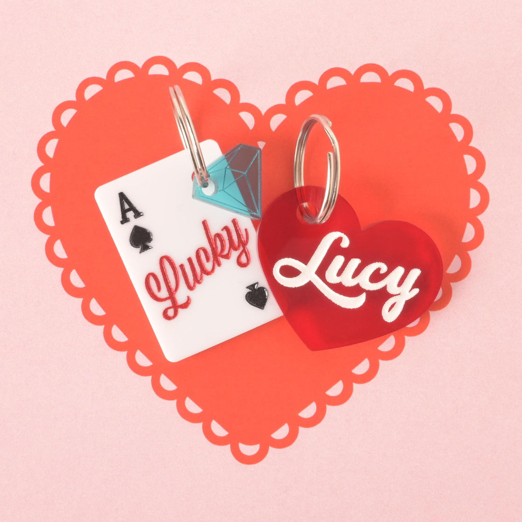 Lucky Ace playing card pet ID tag with jewel mini charm next to a red heart-shaped custom name tag, displayed on scalloped heart background.