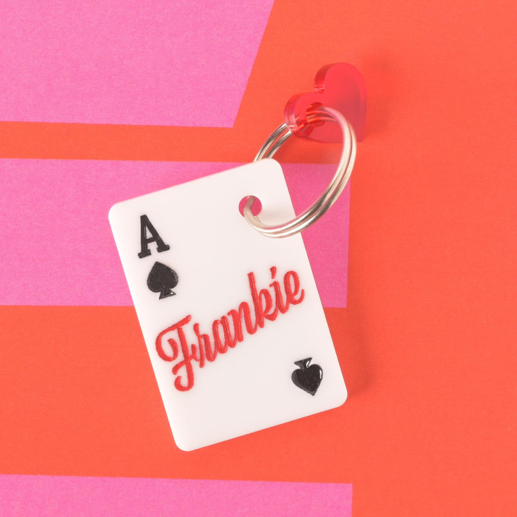 Custom Lucky Ace pet ID tag with the name Frankie engraved in red script, accented with a red heart charm on a bold pink and red backdrop.