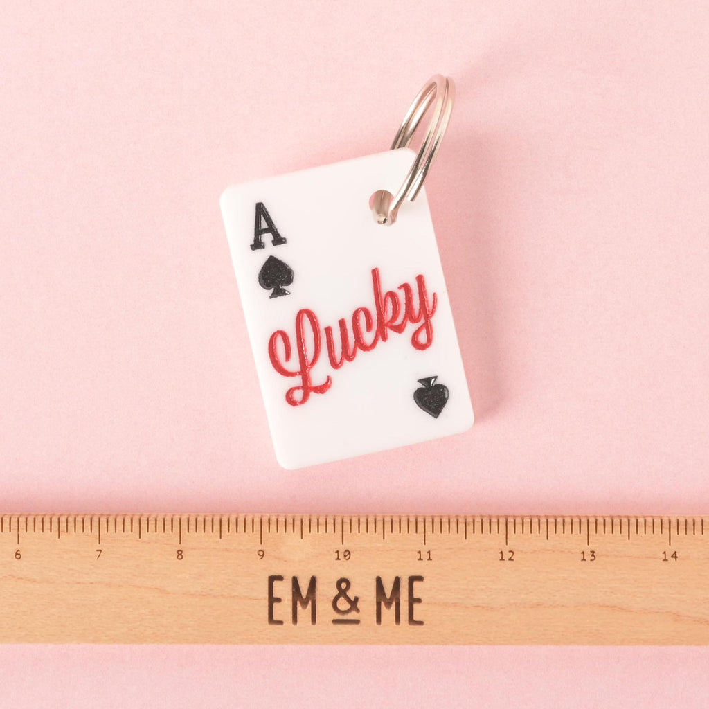 Lucky Ace pet ID tag shaped like a white playing card with red “Lucky” text, shown with a ruler for size reference on a pink background.