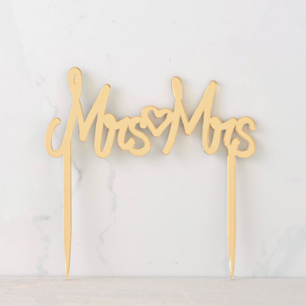 mirror gold cake topper that reads "MRS MRS" with a heart in the middle for wedding. Inclusive LGBTQIA+ celebration.