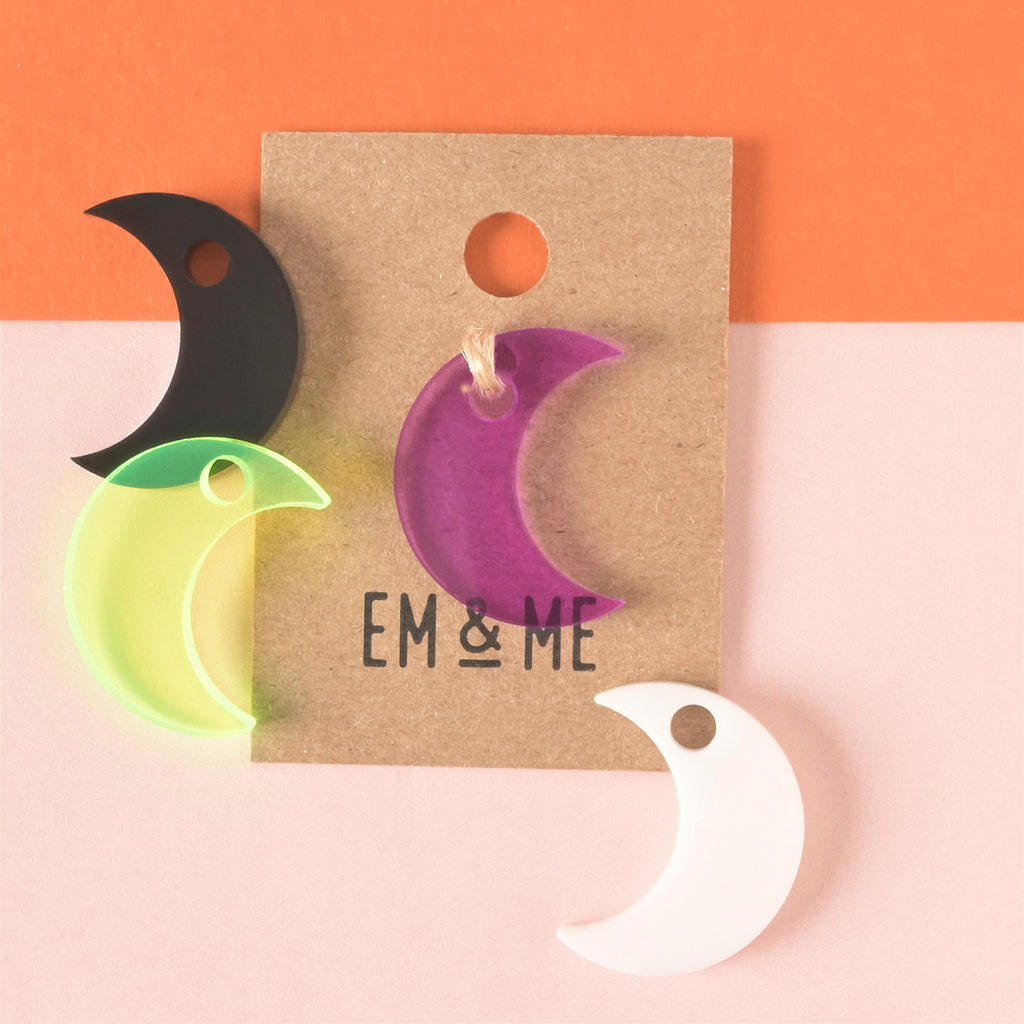 Purple moon-shaped mini charm packaged on brown kraft paper with other moon mini charms surrounding on color blocked background