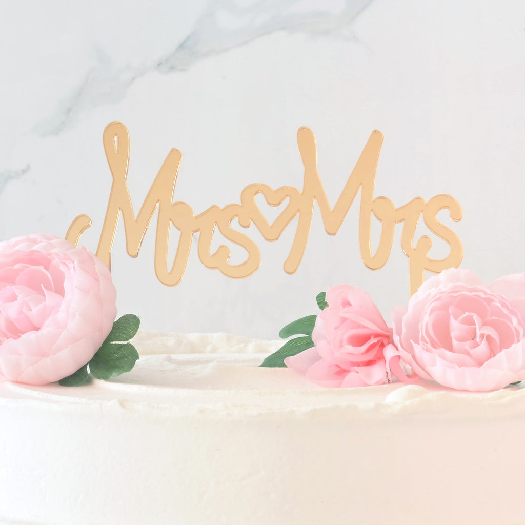Close up of a mirror gold cake topper that reads "MRS MRS" with a heart in the middle in a cake for wedding. Inclusive LGBTQIA+ celebration.