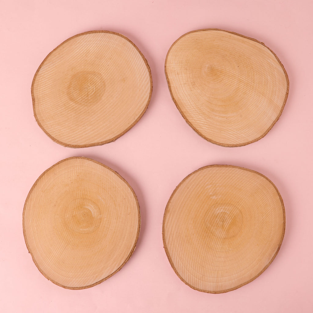 A set of four circular, natural wood slices with visible growth rings and bark edges. These unfinished wood discs are ideal for use as rustic coasters, trivets, or craft blanks.