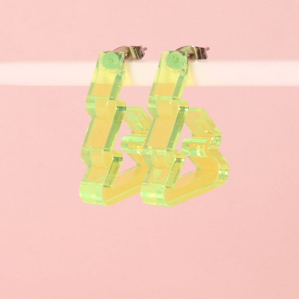A pair of unique holiday earrings shaped like Christmas trees or zig-zags in fluorescent neon yellow-green acrylic. The earrings are lightweight and displayed against a pink background.