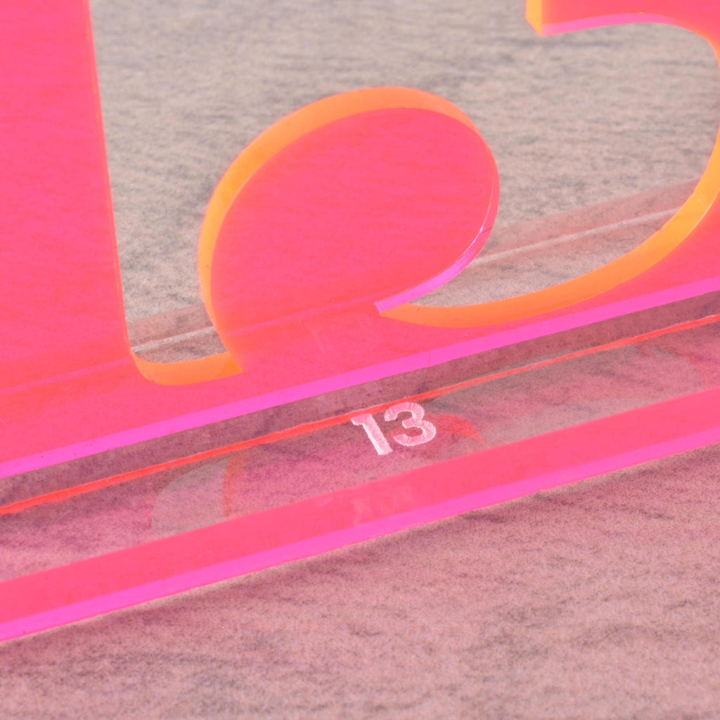 Close-up of fluorescent pink acrylic table number “13” with engraved base detail, trendy wedding reception table decoration.